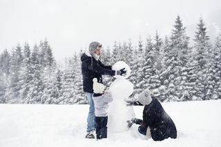 trzyosobowa rodzina buduje bałwana na śniegu