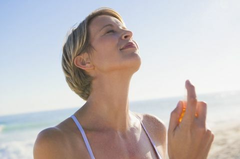 Kobieta rozpylania perfum na jej szyi na plaży