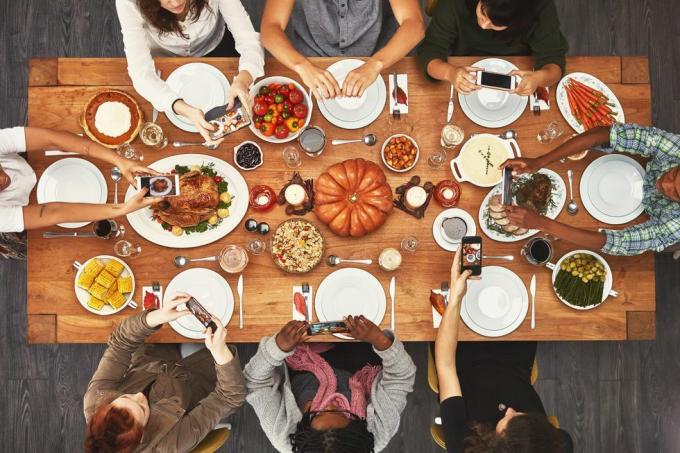 widok z góry na przyjaciół zgromadzonych wokół stołu z okazji Święta Dziękczynienia, którzy robią zdjęcia jedzenia na swoich telefonach, aby opublikować je na Instagramie