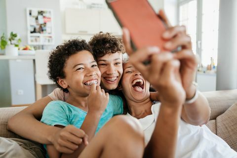 samotna mama bawi się ze swoimi dwoma synami w domu, siedząc na kanapie i robiąc selfie na smartfonie