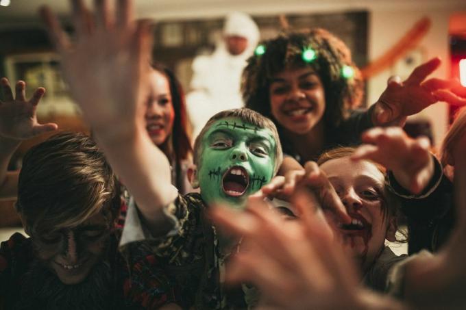 grupa młodych przyjaciół ubranych w kostiumy sięgających do kamery jak zombie