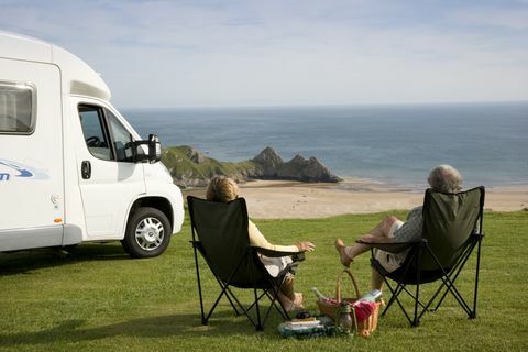 Para z piknikiem relaksującym się na krzesłach obok samochodu kempingowego, z widokiem na zatokę Three Cliffs Bay na półwyspie Gower w Walii., Three Cliffs Bay, Swansea, Walia.