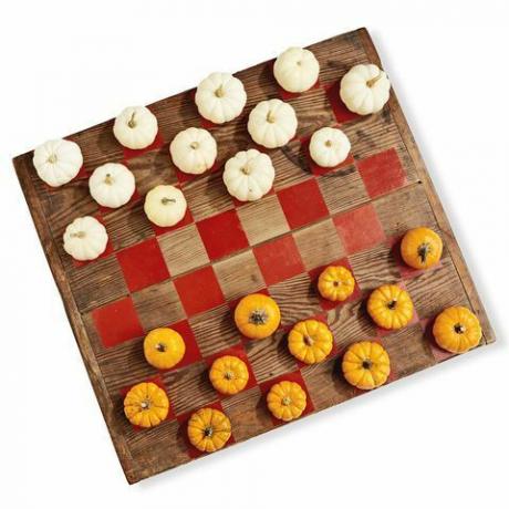drewniana tablica pomalowana na wzór gry w warcaby z wykorzystaniem mini dyń w kolorze białym i pomarańczowym jako elementów do gry
