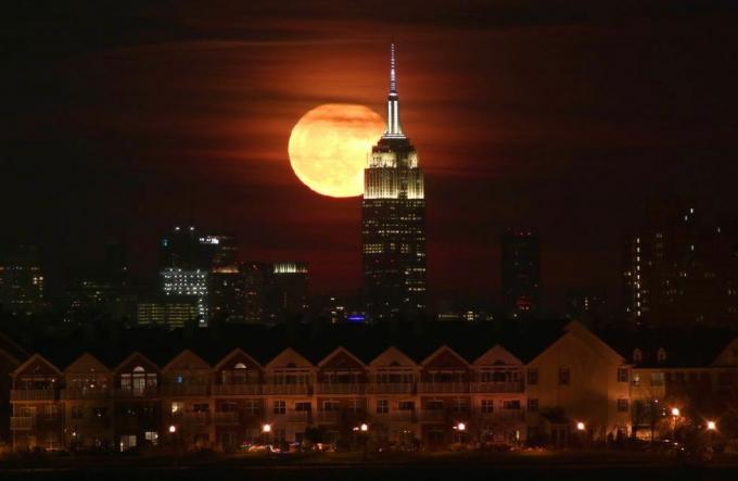 Księżyc w pełni wschodzi za Empire State Building w Nowym Jorku