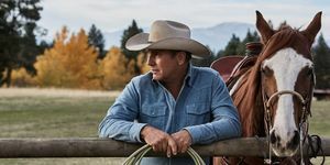 kevin costner w yellowstone obok konia opartego o płot z liną w dłoniach, ubrany w wyblakłą niebieską dżinsową koszulę i beżowy kowbojski kapelusz