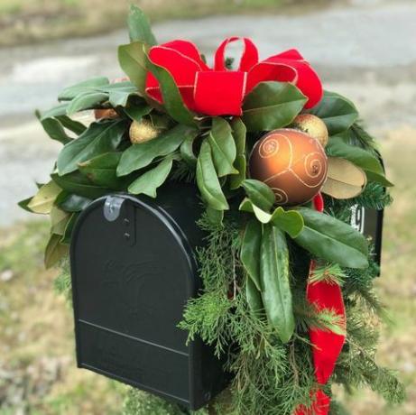 czarna skrzynka pocztowa ozdobiona na święta złotymi bombkami, czerwoną wstążką i mnóstwem zieleni, w tym magnolii i liści cedru