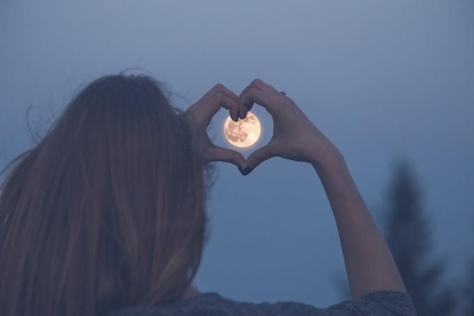 kobieta robi kształt serca z rękami nad księżycem w pełni