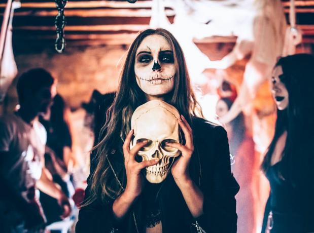 młoda kobieta z makijażem szkieletowym trzymająca czaszkę na imprezie halloween