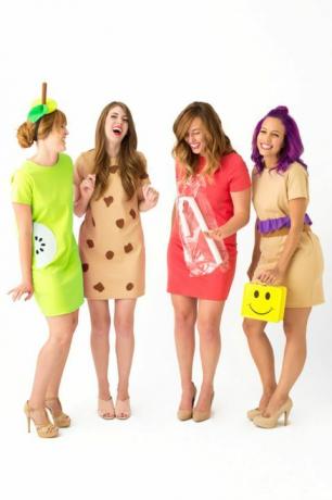 cztery roześmiane kobiety w krótkich sukienkach, ubrane jak „dama na lunch”, jedna nosi pudełko na lunch z żółtym uśmiechem